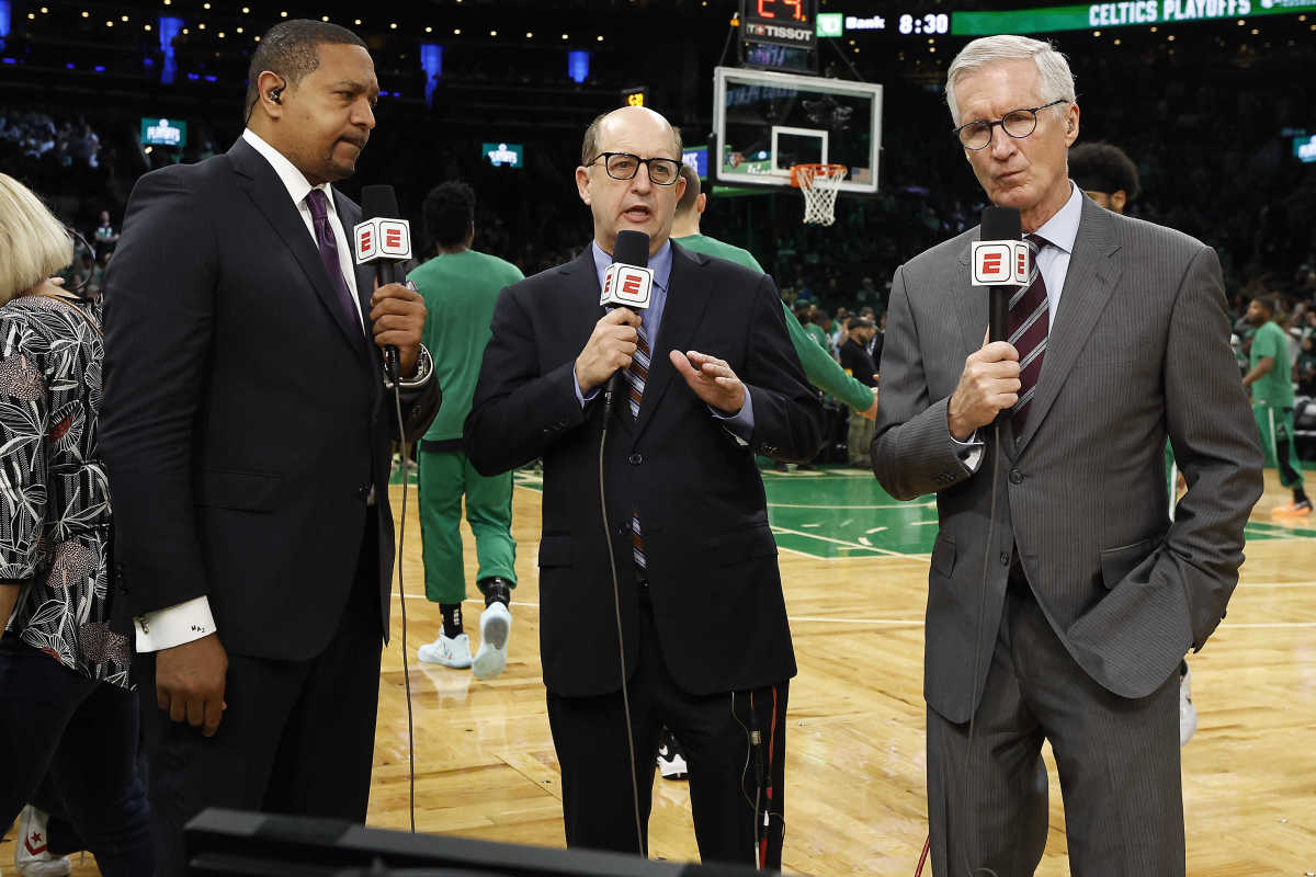 Three ESPN broadcasters stand on the court holding microphones
